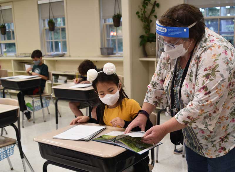 An Elisabeth Morrow School student in a mask reads a book alongside a teacher.