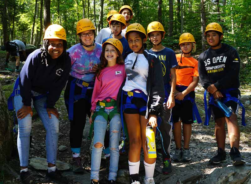 Fifth-, sixth-, and eighth-grade science teacher Dr. Stephanie Nebel and students pose in the woods while wearing hard hats.