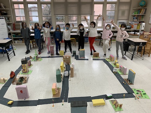 first-grade students cheering while standing behind the play town they've built